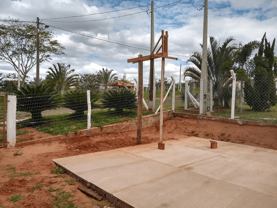 Imagem mostrando a construção de uma tabela de basquete feita artesanalmente, com destaque para o pilar de sustentação e as vigotas de suporte.