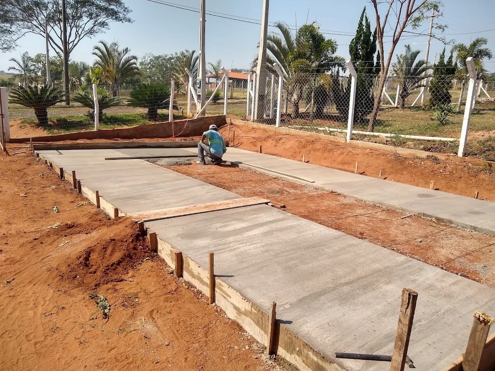 Imagem de um pedreiro espalhando o concreto na quadra de basquete em construção na Chácara Recanto Sofiatti.