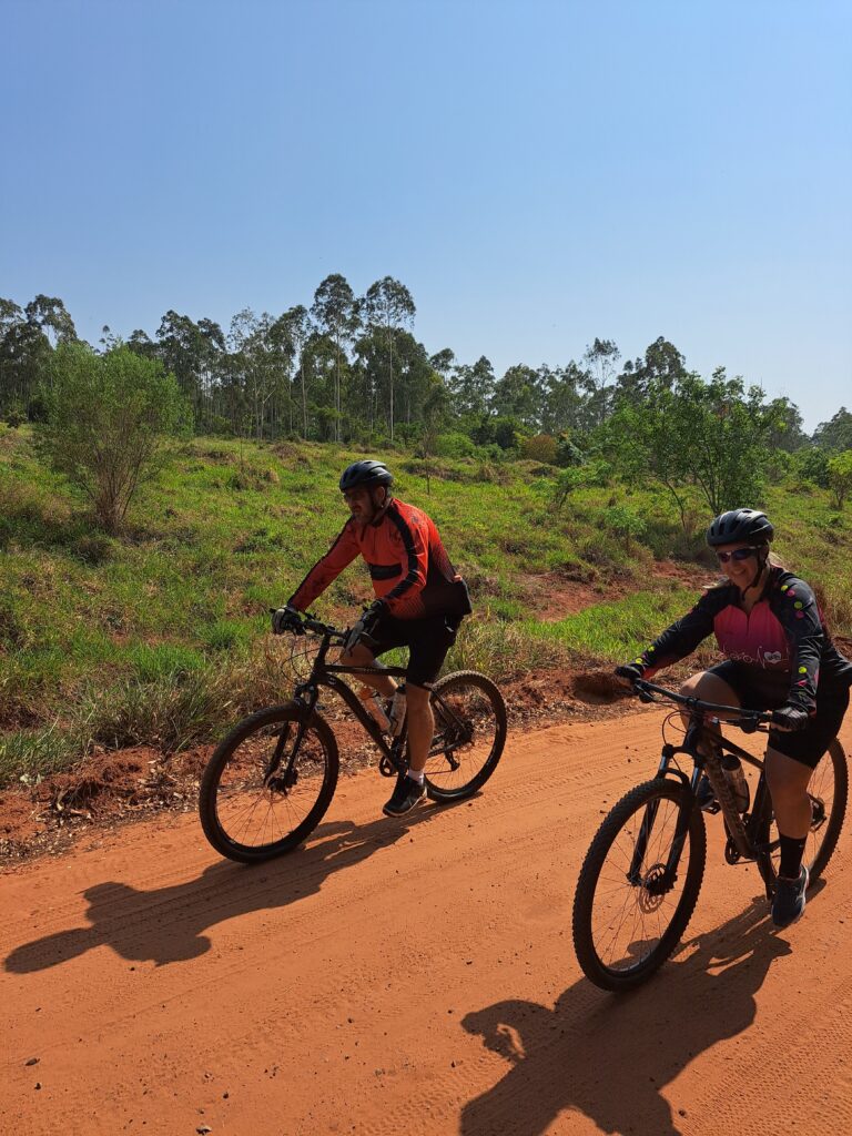 Pais de Laurinha, com sorrisos radiantes, pedalam harmoniosamente lado a lado, celebrando sua aventura na Trilha do Bezerrão e fortalecendo os laços familiares.