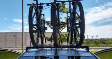 Carro estacionado com três bicicletas no teto, com céu azul ao fundo.