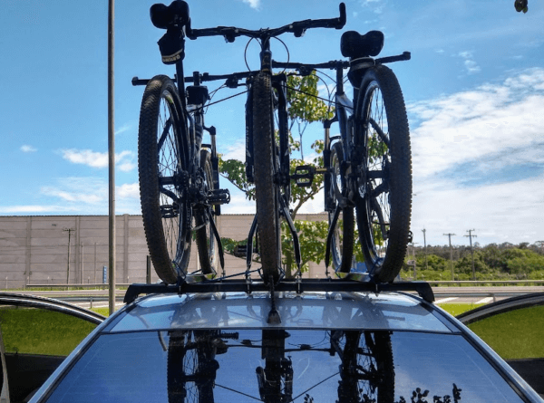 Carro estacionado com três bicicletas no teto, com céu azul ao fundo.