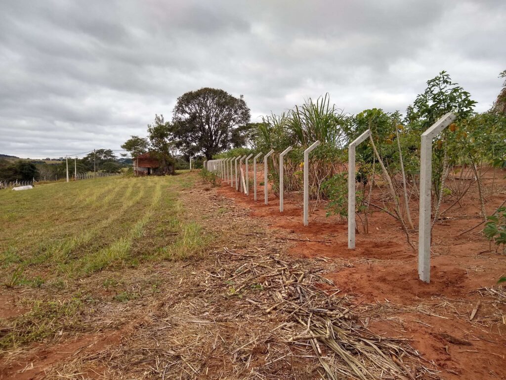 Pilares alinhados formando uma linha ao longo do terreno, destacando a uniformidade e a solidez da cerca de alambrado em construção.