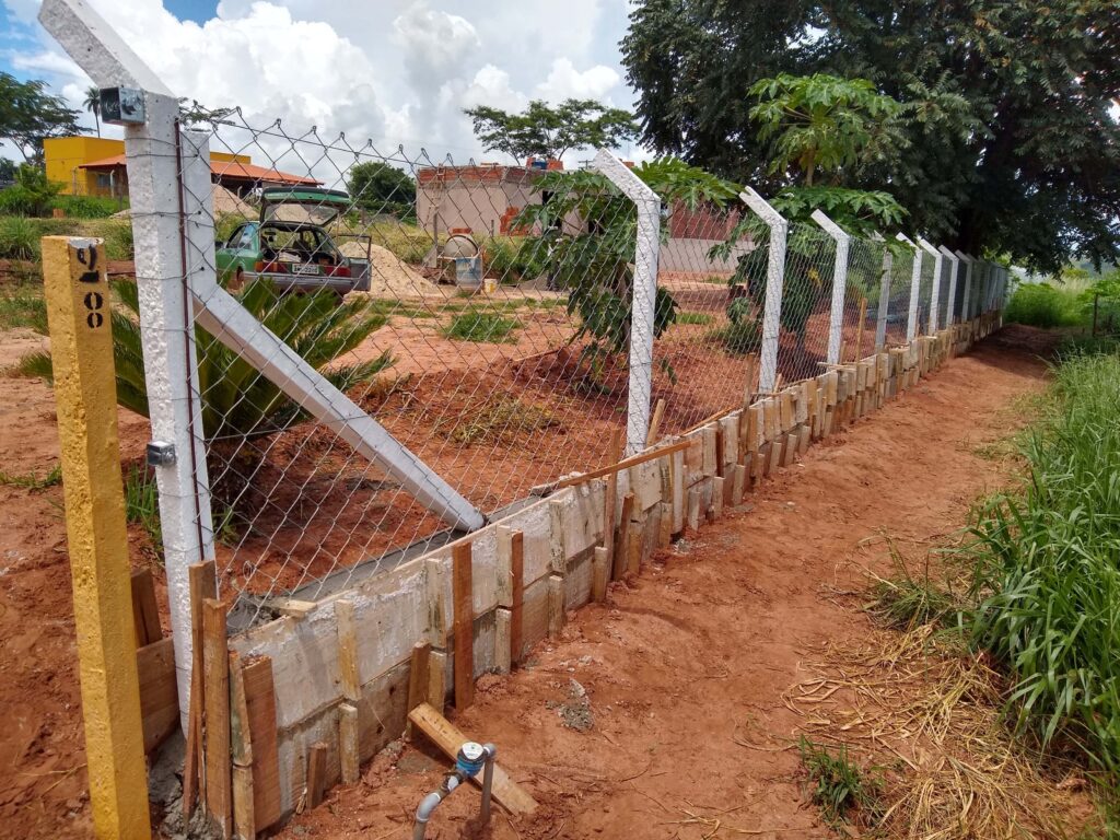 Trabalhadores construindo uma mureta no chão para a fixação segura do alambrado, demonstrando a importância da base sólida na construção da cerca.