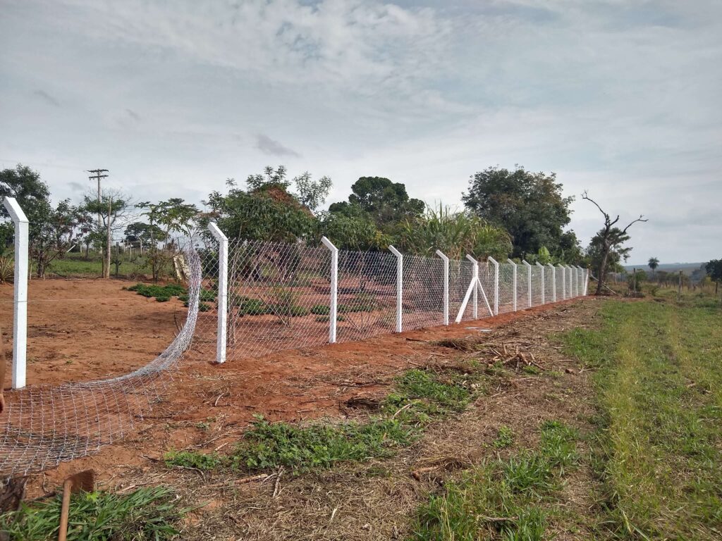 Trabalhador esticando o alambrado e fixando-o nos pilares alinhados, representando um passo fundamental na construção da cerca.