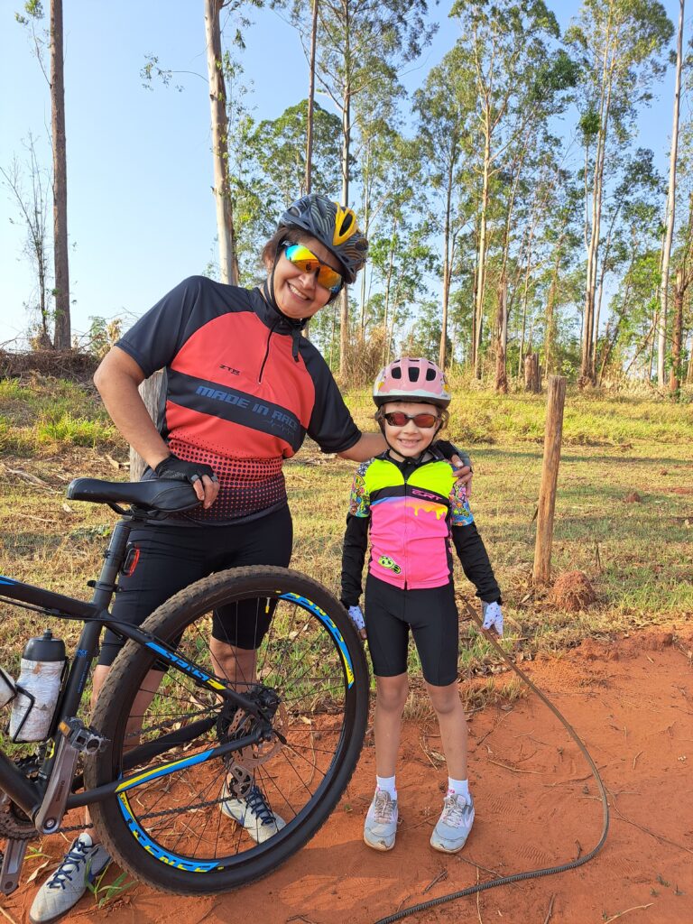 Tia Tina e Laurinha, com sorrisos radiantes, posam ao lado da bicicleta, registrando um momento precioso enquanto exploram a Trilha do Bezerrão.