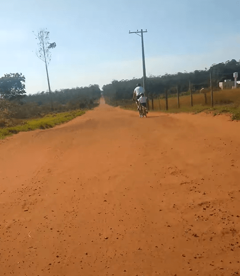 Pai pedala com Laurinha em seu reboque, explorando uma trilha longa e plana, perfeita para iniciantes e crianças.