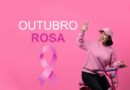 Ciclista demonstrando apoio ao Outubro Rosa com a mão levantada, destacando a relevância da prevenção do câncer de mama.